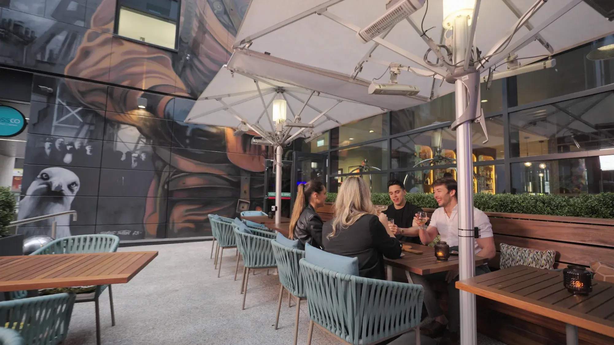 Friends on the Mossco terrace beneath the Shane Sutton mural